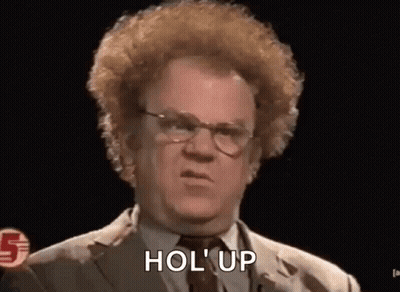 A Man With Curly Hair And Glasses Is Wearing A Suit And Tie And Saying Hol Up . GIF