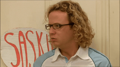 A Man With Curly Hair And Glasses Stands In Front Of A Sign That Says Sas GIF