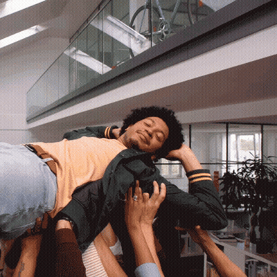 A Man With Curly Hair Is Being Lifted Up By Several People GIF