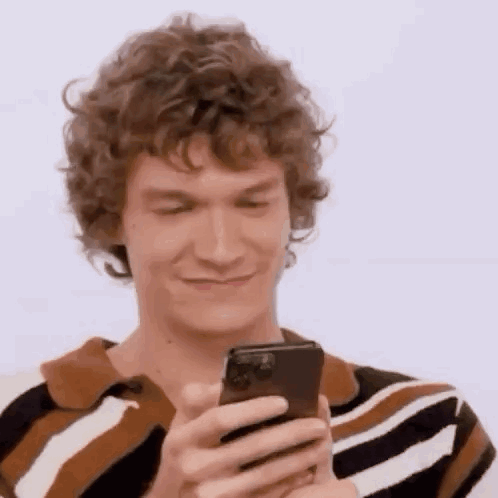 A Man With Curly Hair Is Holding A Cell Phone In His Hand . GIF