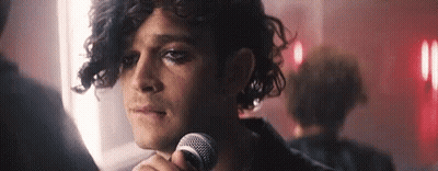 A Man With Curly Hair Is Holding A Microphone In His Hand . GIF