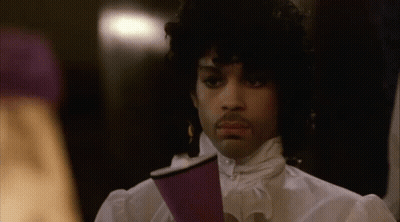 A Man With Curly Hair Is Holding A Purple Cup In His Hand . GIF
