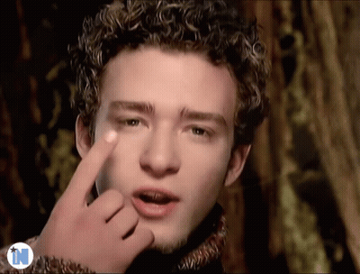 A Man With Curly Hair Is Making A Funny Face With His Finger GIF