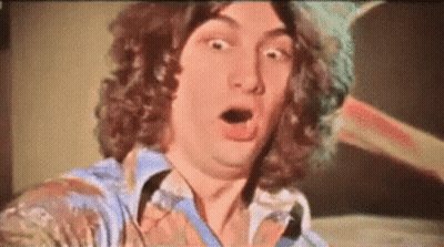 A Man With Curly Hair Is Making A Surprised Face With His Mouth Open GIF