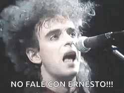 A Man With Curly Hair Is Singing Into A Microphone In Spanish . GIF