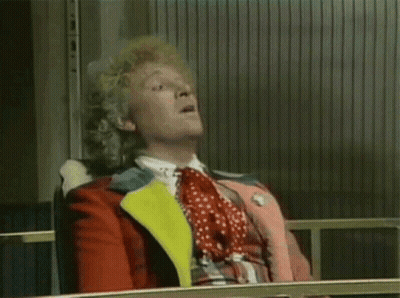 A Man With Curly Hair Is Sitting In A Chair And Making A Funny Face . GIF