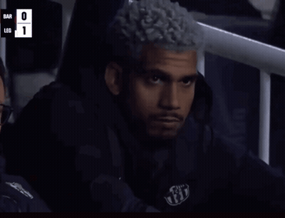 A Man With Curly Hair Is Sitting In A Stadium Watching A Game With The Score Bar 0 Leg 1 GIF