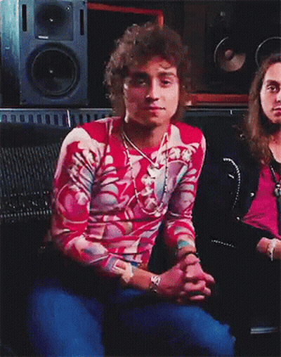 A Man With Curly Hair Is Sitting In Front Of A Speaker GIF
