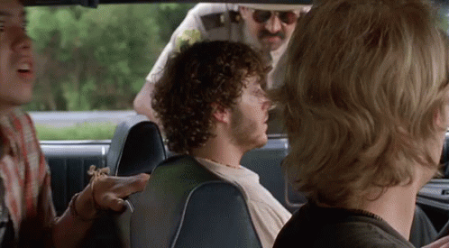 A Man With Curly Hair Is Sitting In The Back Seat Of A Car Talking To Another Man . GIF
