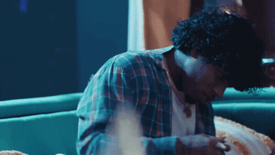 A Man With Curly Hair Is Sitting On A Couch Looking Down GIF
