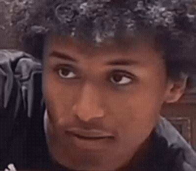 A Man With Curly Hair Is Smiling And Making A Funny Face With His Mouth Open . GIF