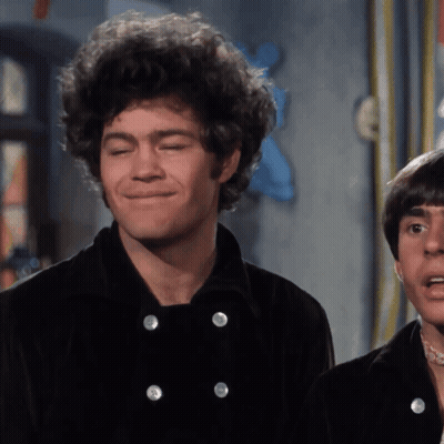 A Man With Curly Hair Is Smiling While Wearing A Black Jacket GIF