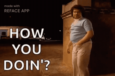 A Man With Curly Hair Is Standing In Front Of A Building . GIF