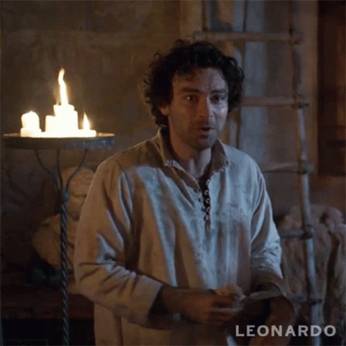 A Man With Curly Hair Is Standing In Front Of A Candle Holder With The Name Leonardo On The Bottom Right GIF