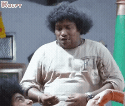 A Man With Curly Hair Is Standing In Front Of A Green Wall And Talking To Another Man . GIF