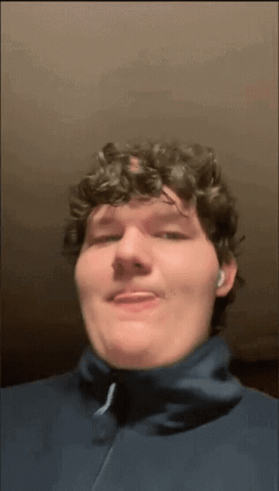 A Man With Curly Hair Is Wearing A Blue Jacket And Ear Buds GIF