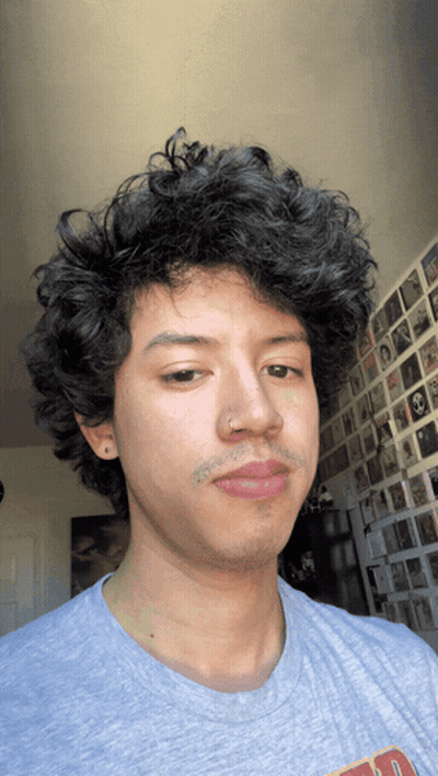 A Man With Curly Hair Is Wearing A Grey Shirt That Says ' A ' On The Front GIF