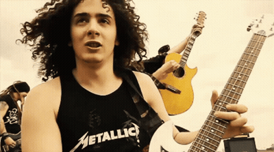A Man With Curly Hair Is Wearing A Metallica Tank Top GIF