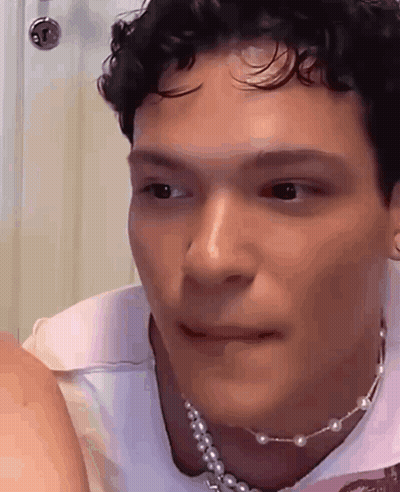 A Man With Curly Hair Is Wearing A Pearl Necklace And Making A Funny Face . GIF