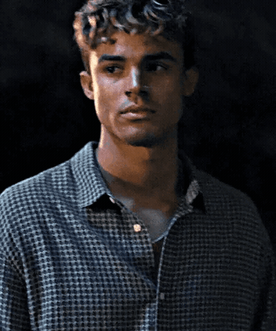 A Man With Curly Hair Is Wearing A Plaid Shirt And A Necklace GIF