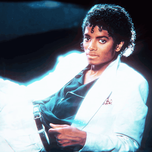 A Man With Curly Hair Is Wearing A White Jacket And Black Shirt GIF
