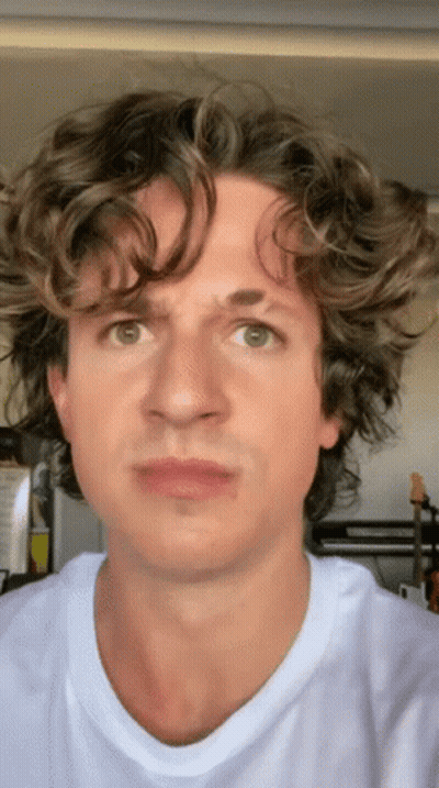 A Man With Curly Hair Is Wearing A White T-Shirt And Making A Funny Face GIF