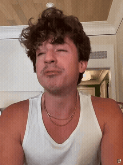 A Man With Curly Hair Is Wearing A White Tank Top And A Gold Necklace GIF