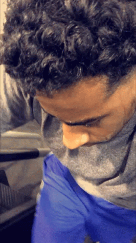 A Man With Curly Hair Is Wearing Blue Shorts And A Grey Shirt GIF