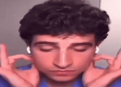 A Man With Curly Hair Is Wearing Headphones And Making A Funny Face With His Hands . GIF