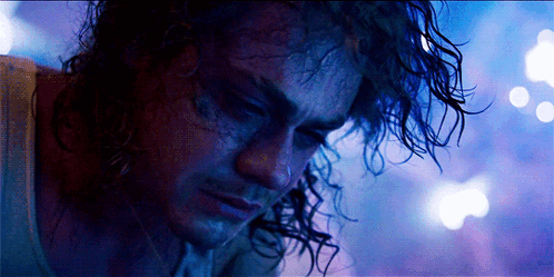 A Man With Curly Hair Looks Down At Something GIF