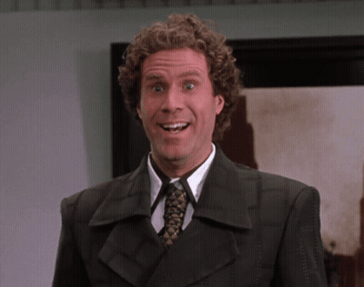 A Man With Curly Hair Wearing A Suit And Tie Smiles GIF