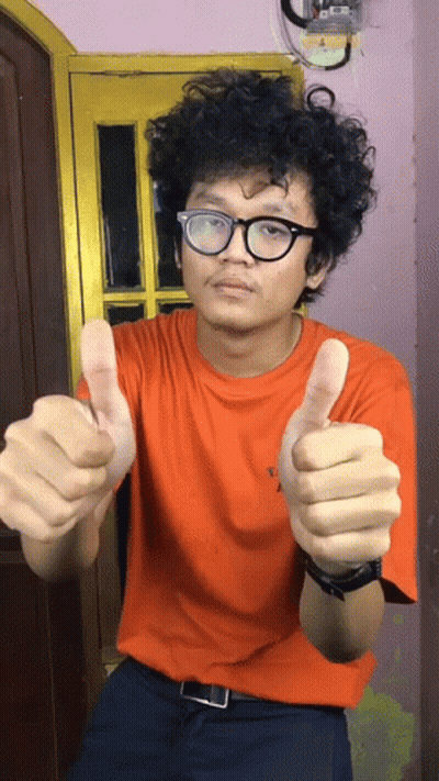 A Man With Curly Hair Wearing Glasses And An Orange Shirt Giving A Thumbs Up GIF