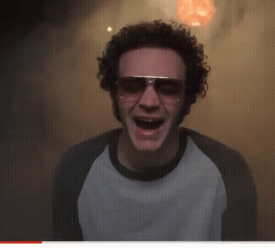 A Man With Curly Hair Wearing Sunglasses And A White Shirt With His Mouth Open GIF