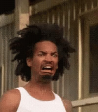 A Man With Dreadlocks And A Beard Is Making A Funny Face While Wearing A White Tank Top . GIF
