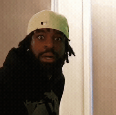 A Man With Dreadlocks And A Beard Wearing A White Hat And A Black Hoodie Is Making A Funny Face . GIF