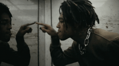 A Man With Dreadlocks And A Chain Around His Neck Looks At Himself In A Mirror GIF