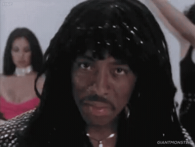 A Man With Dreadlocks And A Mustache Is Standing In Front Of Two Women In Dresses . GIF