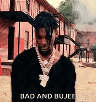 A Man With Dreadlocks And A Necklace Is Standing In Front Of A Building Smoking A Cigarette . GIF