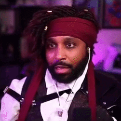 A Man With Dreadlocks And A Red Headband Is Wearing A Tuxedo And Ear Buds . GIF