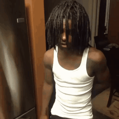 A Man With Dreadlocks And A White Tank Top Is Standing In Front Of A Refrigerator . GIF