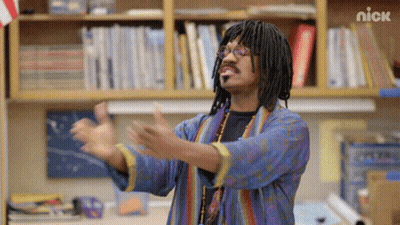 A Man With Dreadlocks And Glasses Is Standing In Front Of A Bookshelf With The Nick Logo On It GIF
