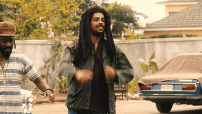 A Man With Dreadlocks Is Dancing In Front Of A Bob Marley Sign GIF