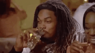 A Man With Dreadlocks Is Drinking A Glass Of Water While Sitting At A Table . GIF