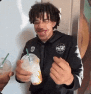 A Man With Dreadlocks Is Drinking From A Plastic Cup With A Straw GIF