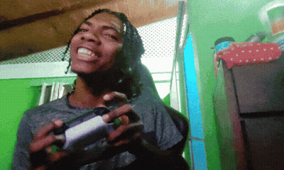 A Man With Dreadlocks Is Holding A Game Controller And Smiling GIF