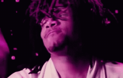 A Man With Dreadlocks Is Holding A Purple Object In His Hand And Making A Funny Face . GIF