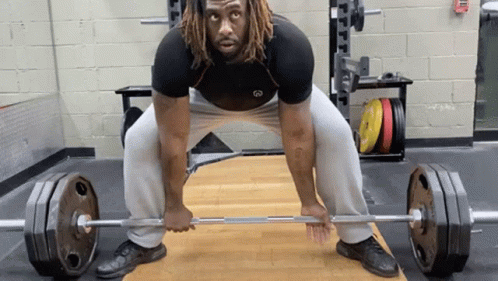 A Man With Dreadlocks Is Lifting A Barbell In A Gym . GIF