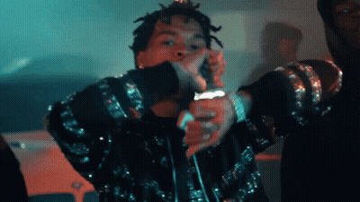 A Man With Dreadlocks Is Singing Into A Microphone While Wearing A Black Jacket GIF