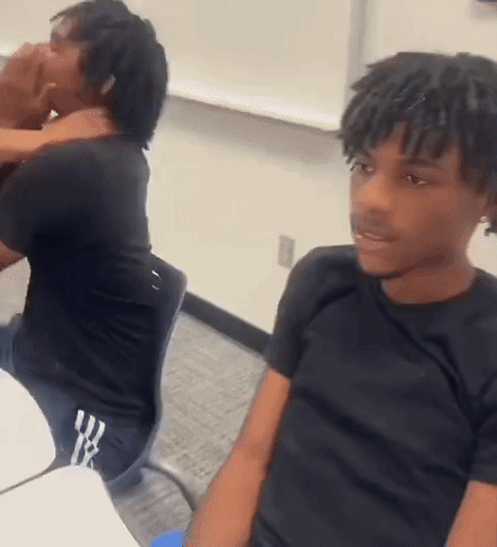 A Man With Dreadlocks Is Sitting At A Desk In A Classroom . GIF