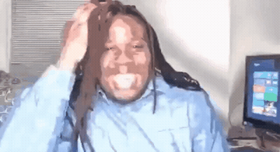 A Man With Dreadlocks Is Sitting In Front Of A Computer And Holding His Hair . GIF